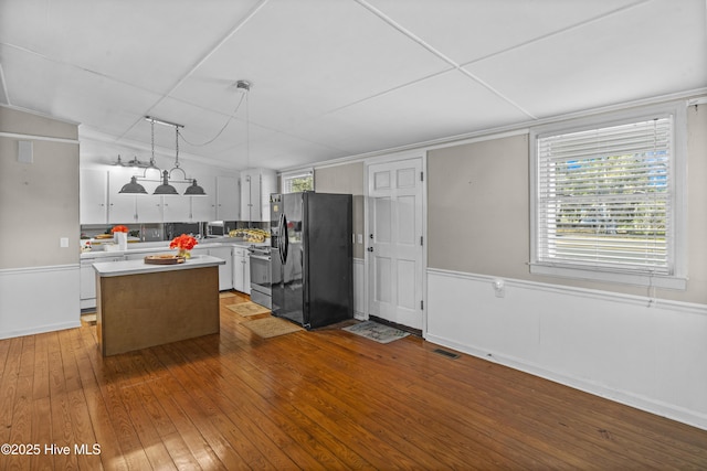 kitchen featuring light wood-type flooring, black fridge, a kitchen island, white cabinetry, and hanging light fixtures