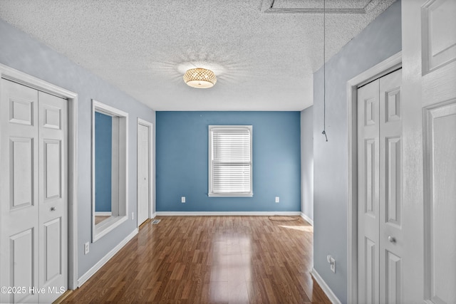 unfurnished bedroom with a textured ceiling, two closets, and hardwood / wood-style flooring