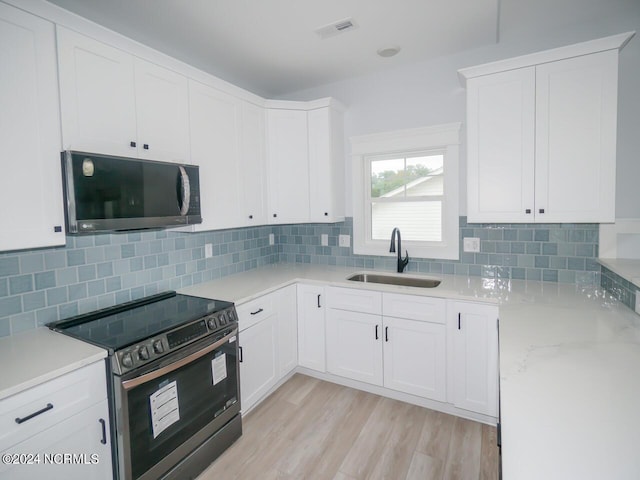 kitchen featuring tasteful backsplash, white cabinetry, sink, and black electric range