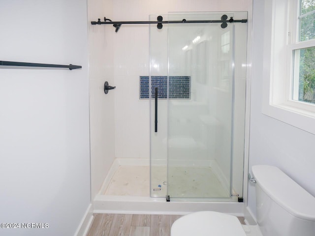 bathroom with toilet, a shower with door, and wood-type flooring