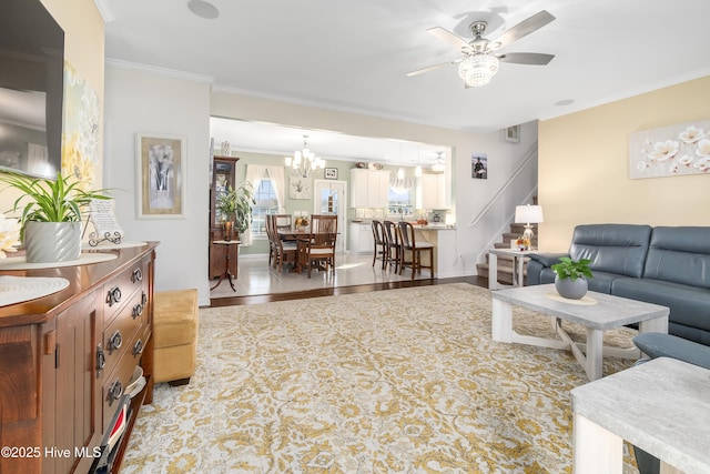 living room with ceiling fan with notable chandelier, ornamental molding, and light wood-type flooring