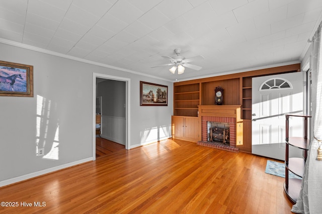 unfurnished living room with a brick fireplace, ornamental molding, built in shelves, ceiling fan, and light hardwood / wood-style floors