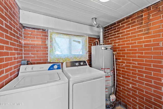 laundry room featuring washer and dryer, water heater, and brick wall