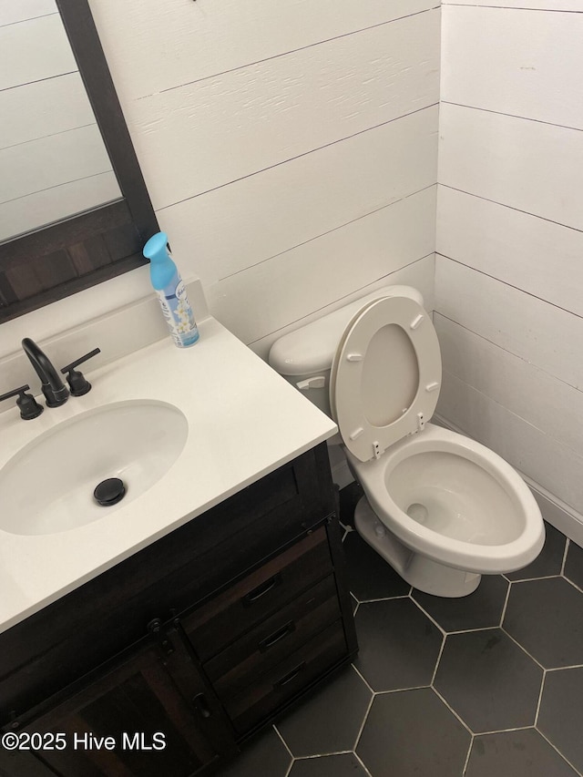 bathroom with tile patterned floors, wooden walls, vanity, and toilet