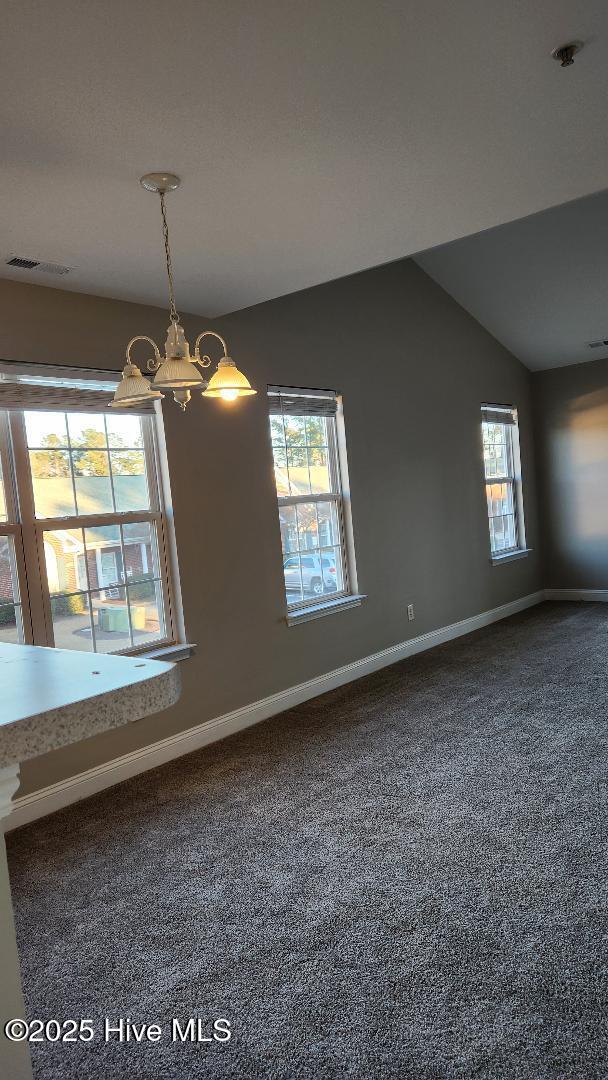 spare room with carpet flooring, vaulted ceiling, an inviting chandelier, and a healthy amount of sunlight