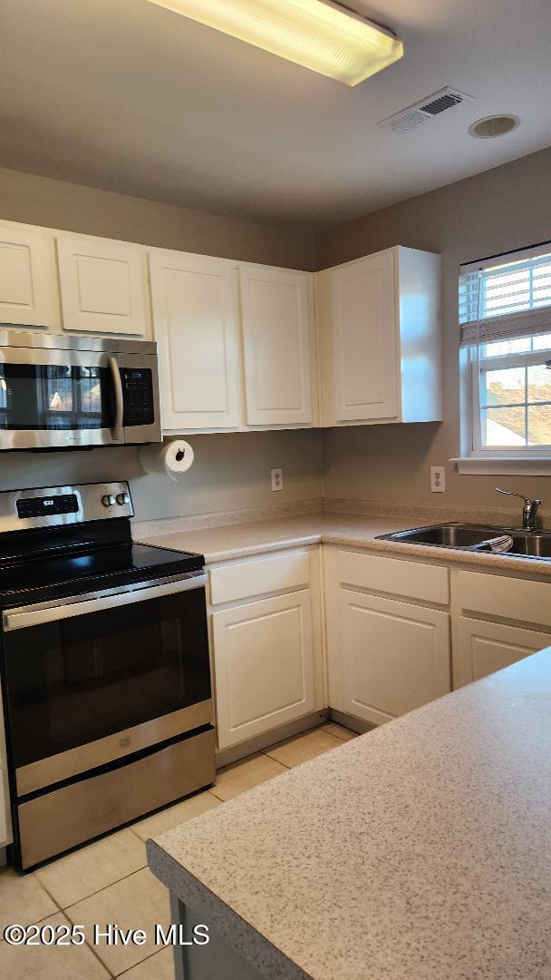 kitchen with white cabinetry, sink, light tile patterned flooring, and appliances with stainless steel finishes