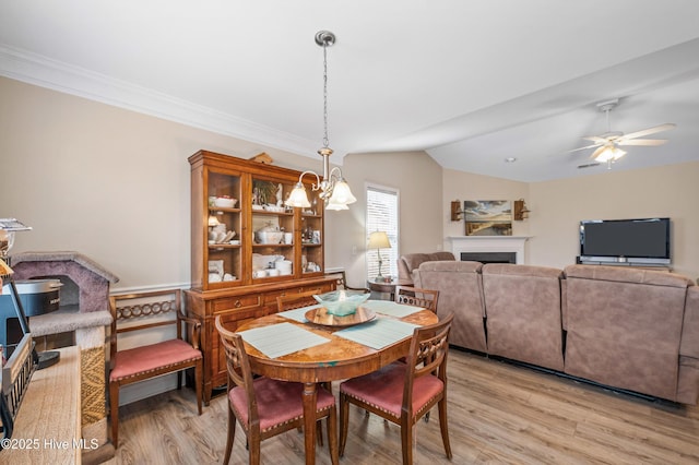 dining space featuring vaulted ceiling, ornamental molding, ceiling fan with notable chandelier, and light wood-type flooring