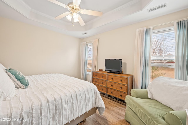 bedroom with a tray ceiling, crown molding, ceiling fan, and light hardwood / wood-style floors