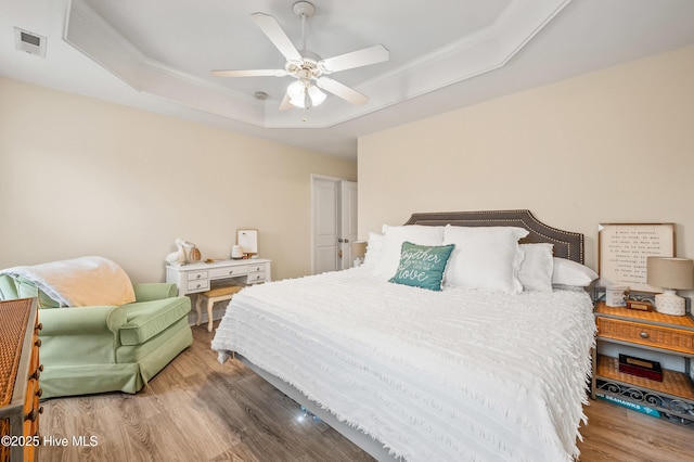 bedroom featuring ceiling fan, wood-type flooring, and a tray ceiling