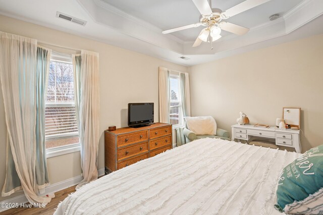 bedroom with multiple windows, light wood-type flooring, a tray ceiling, and ceiling fan