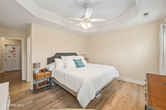 bedroom with light wood-type flooring, a tray ceiling, and ceiling fan