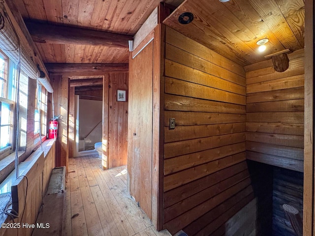 hall featuring wood walls, beam ceiling, light hardwood / wood-style floors, and wooden ceiling