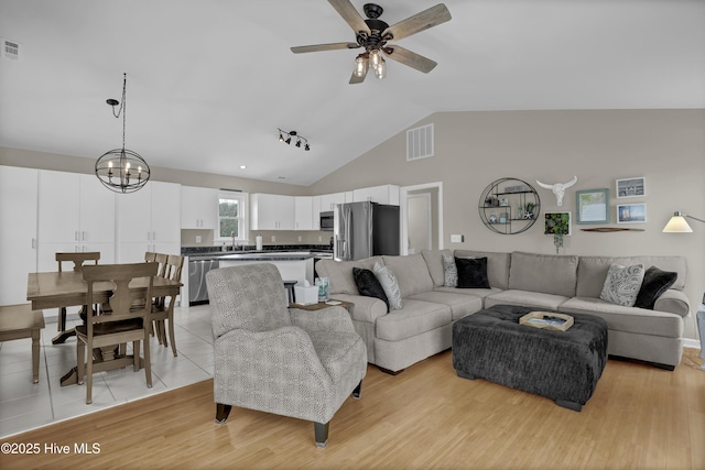 living room featuring sink, light wood-type flooring, vaulted ceiling, and ceiling fan with notable chandelier