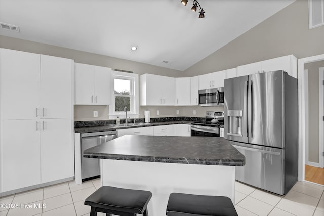 kitchen with white cabinets, vaulted ceiling, stainless steel appliances, a kitchen island, and sink