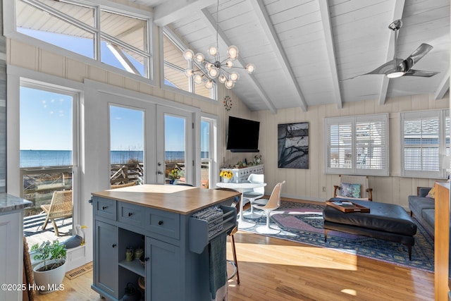 kitchen featuring beam ceiling, french doors, a water view, ceiling fan with notable chandelier, and light wood-type flooring