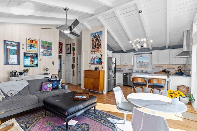 living room with lofted ceiling with beams, light hardwood / wood-style floors, sink, and ceiling fan with notable chandelier