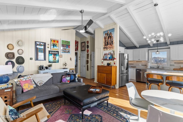 living room with ceiling fan with notable chandelier, lofted ceiling with beams, light hardwood / wood-style floors, and sink