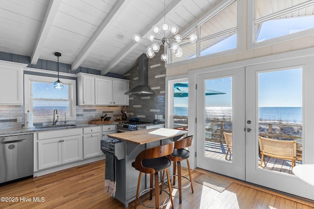 kitchen with french doors, a water view, wall chimney range hood, sink, and appliances with stainless steel finishes