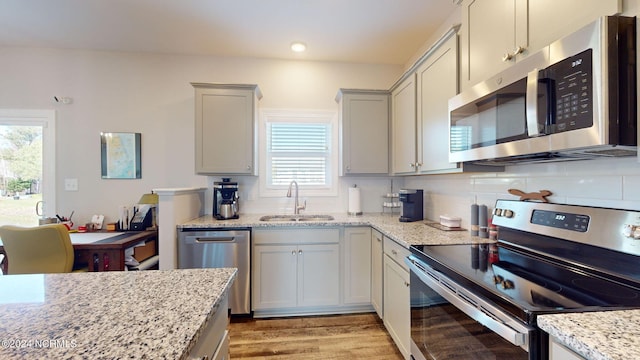 kitchen featuring sink, light stone countertops, stainless steel appliances, and a wealth of natural light