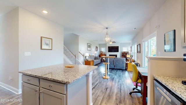 kitchen with hanging light fixtures, light hardwood / wood-style flooring, stainless steel dishwasher, ceiling fan, and light stone counters