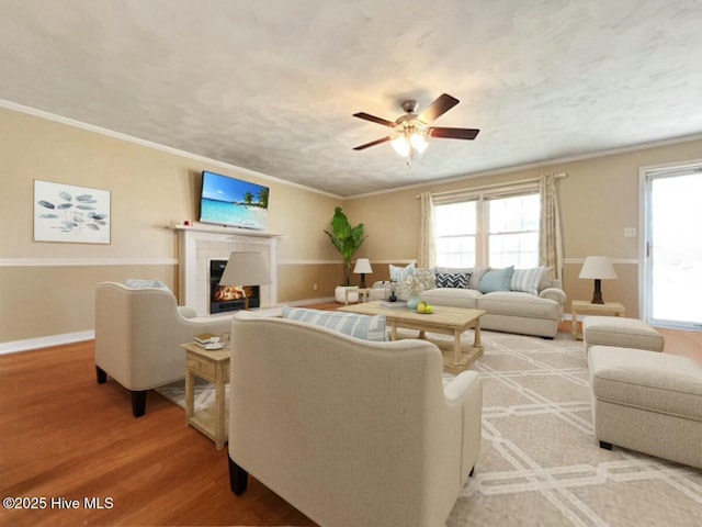 living room featuring a fireplace, light hardwood / wood-style flooring, ceiling fan, and crown molding