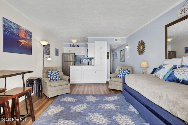 bedroom with a textured ceiling, dark wood-type flooring, stainless steel refrigerator, and crown molding