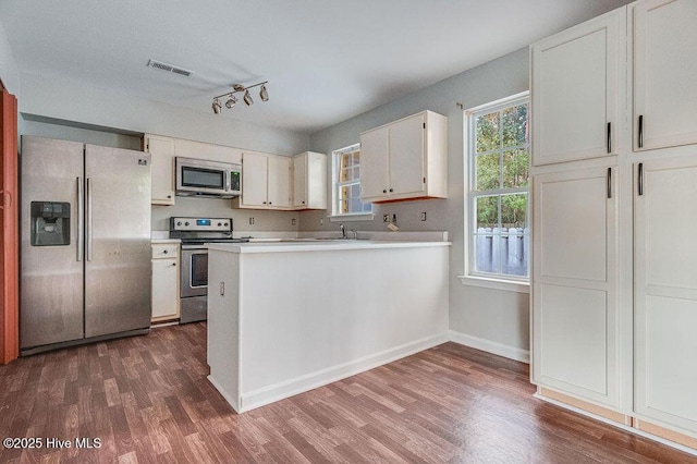 kitchen with rail lighting, white cabinets, dark wood-type flooring, and appliances with stainless steel finishes