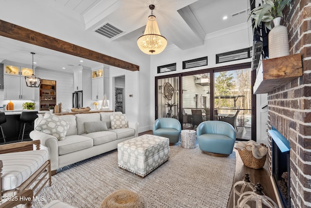 living room with beamed ceiling, a chandelier, hardwood / wood-style floors, and a brick fireplace