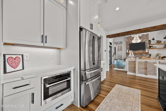 kitchen with appliances with stainless steel finishes, light wood-type flooring, white cabinetry, and light stone counters