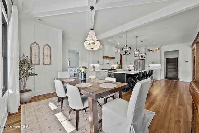 dining room featuring sink, beamed ceiling, light hardwood / wood-style floors, and a notable chandelier