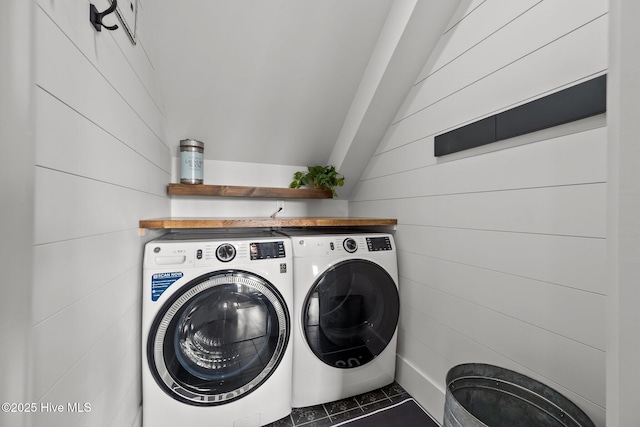 washroom with washer and dryer, dark tile patterned floors, and wooden walls