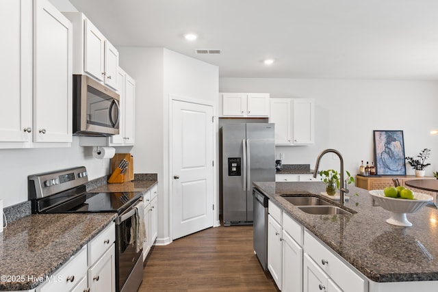 kitchen featuring dark stone countertops, sink, white cabinetry, a kitchen island with sink, and appliances with stainless steel finishes