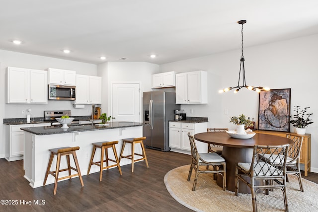 kitchen featuring hanging light fixtures, a kitchen island with sink, dark wood-type flooring, stainless steel appliances, and white cabinets