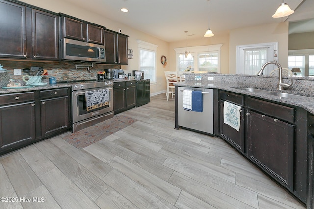 kitchen with a sink, stainless steel appliances, dark brown cabinets, and hanging light fixtures