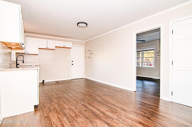 kitchen with light stone countertops, tasteful backsplash, ornamental molding, wood-type flooring, and white cabinetry