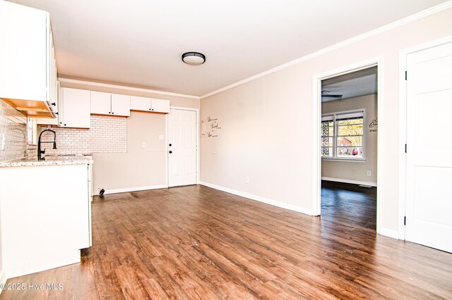 kitchen with white cabinets, hardwood / wood-style flooring, decorative backsplash, ornamental molding, and light stone counters