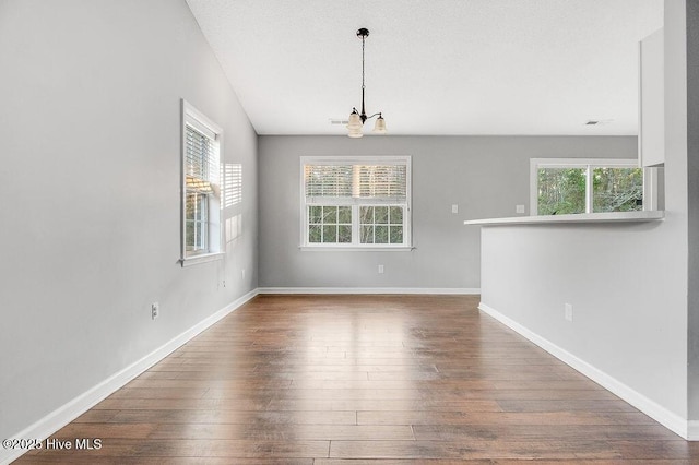 empty room with hardwood / wood-style floors, an inviting chandelier, and a wealth of natural light