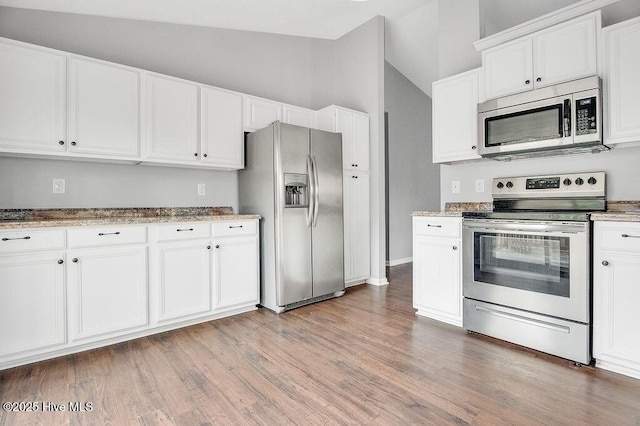 kitchen featuring vaulted ceiling, light stone countertops, appliances with stainless steel finishes, light hardwood / wood-style floors, and white cabinetry