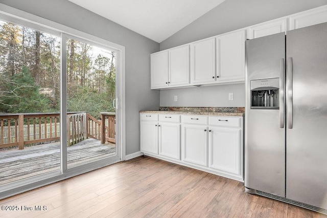 kitchen featuring stainless steel fridge, dark stone counters, vaulted ceiling, light hardwood / wood-style flooring, and white cabinetry