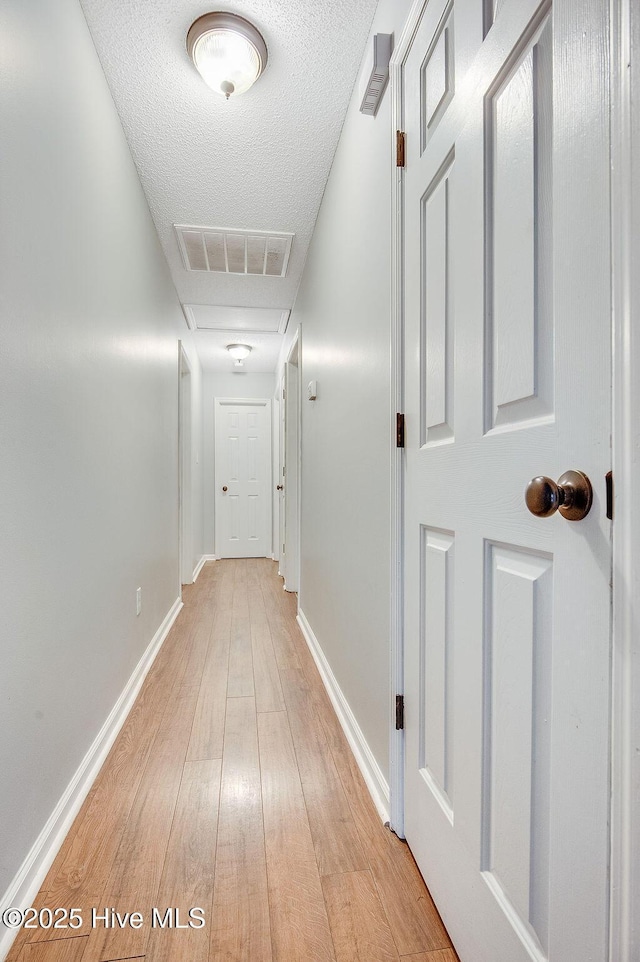 hall with light wood-type flooring and a textured ceiling