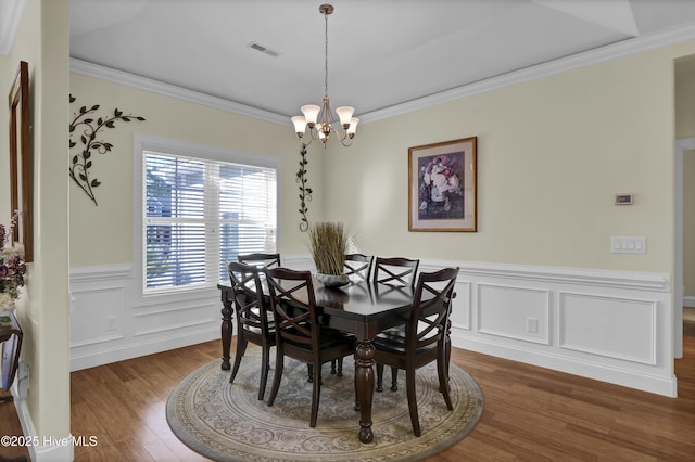 dining space with dark wood-type flooring, crown molding, and an inviting chandelier