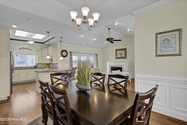 dining area with crown molding, wood-type flooring, lofted ceiling with skylight, and ceiling fan with notable chandelier