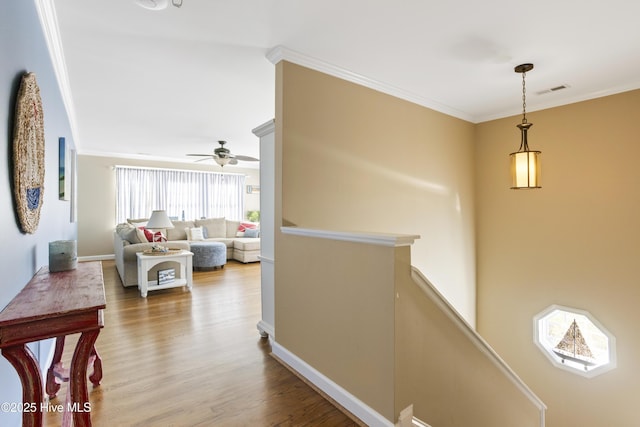 hall featuring visible vents, ornamental molding, an upstairs landing, wood finished floors, and baseboards