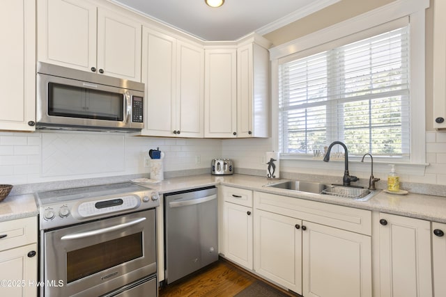 kitchen with white cabinets, a sink, stainless steel appliances, crown molding, and backsplash