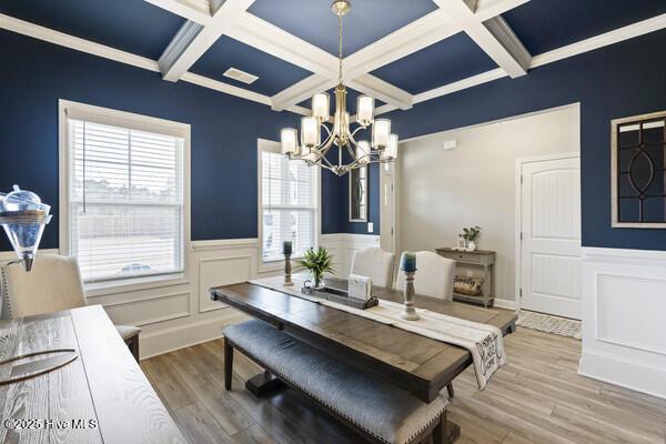 dining space with beamed ceiling, an inviting chandelier, ornamental molding, hardwood / wood-style flooring, and coffered ceiling