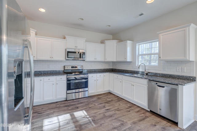 kitchen featuring appliances with stainless steel finishes, sink, light hardwood / wood-style flooring, dark stone countertops, and white cabinetry