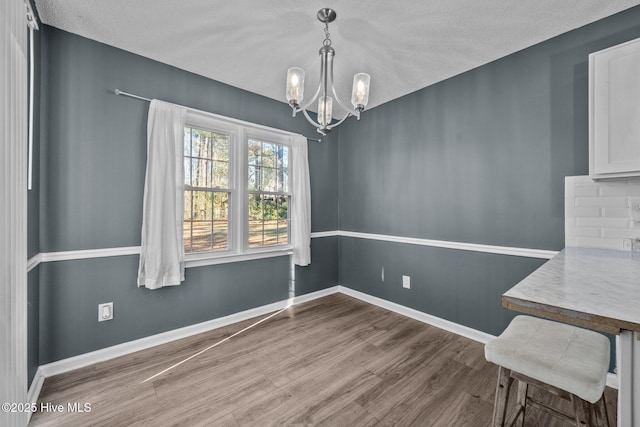 unfurnished dining area featuring hardwood / wood-style floors, a notable chandelier, and a textured ceiling