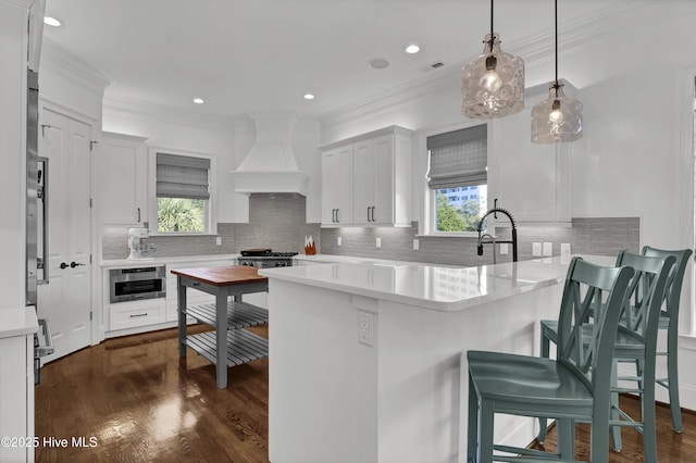 kitchen with kitchen peninsula, a kitchen bar, custom exhaust hood, decorative light fixtures, and white cabinetry