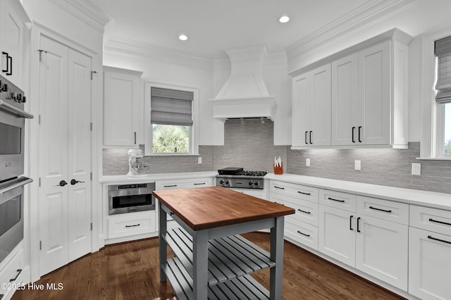 kitchen featuring butcher block countertops, custom exhaust hood, white cabinetry, and crown molding