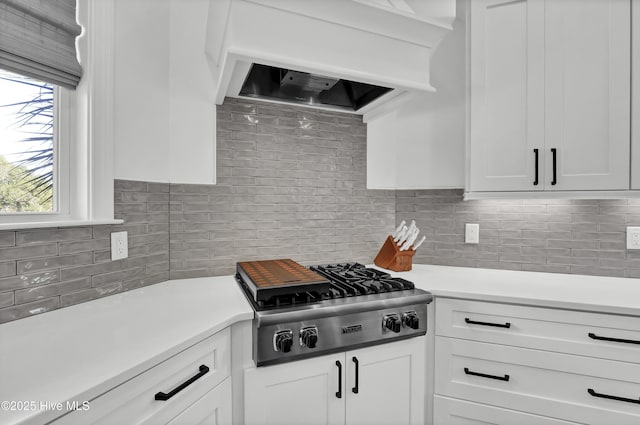 kitchen featuring ventilation hood, stainless steel gas stovetop, white cabinetry, and tasteful backsplash